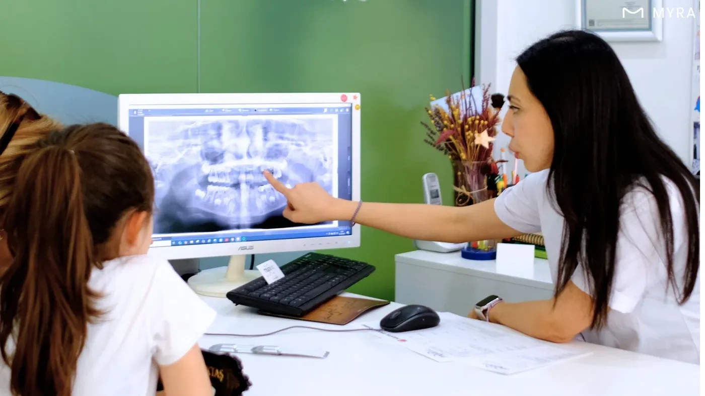 Çocuğunu tedaviye getiren ebeveyn ve açıklama yapan pedodontist sahnesi